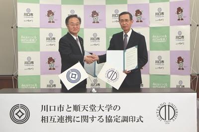 協定調印式で奥ノ木信夫川口市長(左)と木南英紀順天堂大学学長(右)が握手を交わしている写真