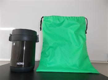 元郷学校給食センターで提供している食物アレルギー対応食に使用する個別容器の写真。黒い保温容器に給食を盛り付け、緑の袋に入れて学校へ届けられます。