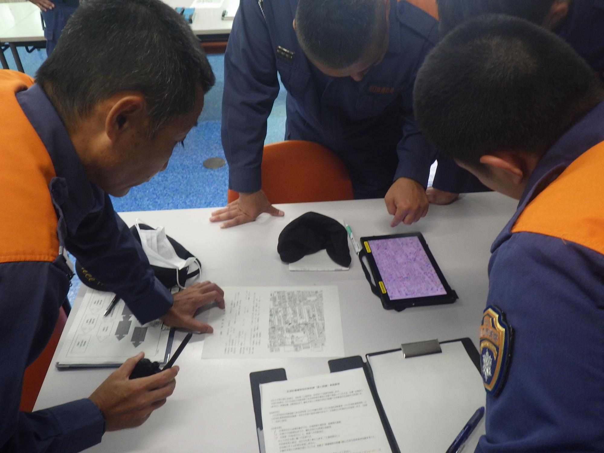 災害現場（仮想）を示した指令書とタブレットを使用し災害現場までのルート、現場付近の消火栓の状況、隊長からの隊員への活動指示など短時間活動方針を決定します。