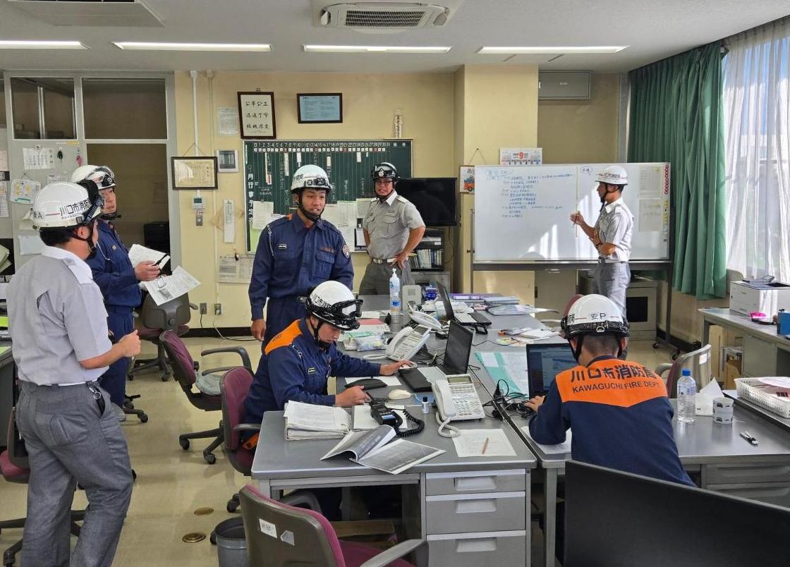 安行分署の事務所内でヘルメットをかぶり、情報収集をしてる消防隊と救急隊7人の写真