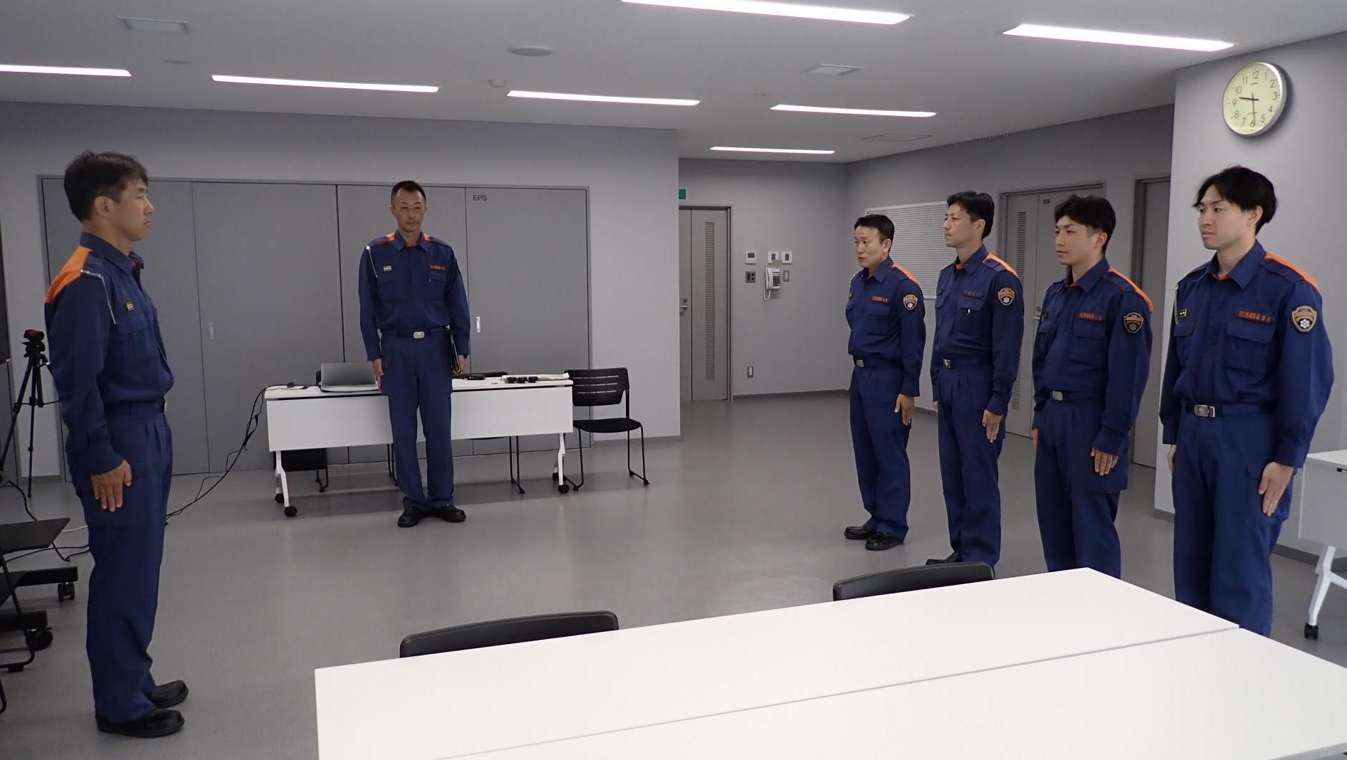 室内で、整列する消防隊4名と前に立つ東消防署の消防課長の写真