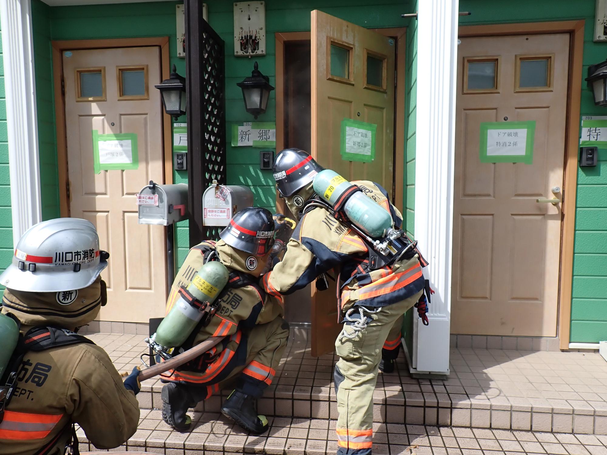 消防隊員3名がホースを持ってドアから進入しようとしている写真