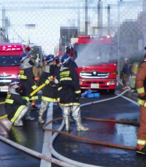 路上で消防用ホースを使って放水している4人の消防団員の写真