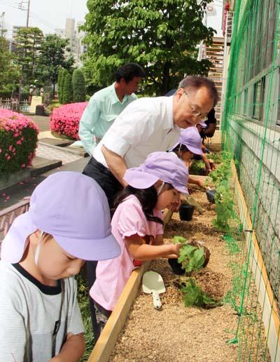「グリーンカーテン設置啓発事業」本庁舎苗植え式で子供たちと苗植えをする市長の写真
