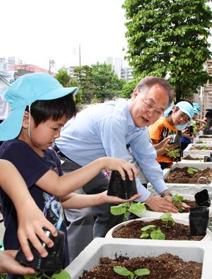 「グリーンカーテン設置啓発事業」本庁舎苗植え式で参加者と苗植えをする市長の写真